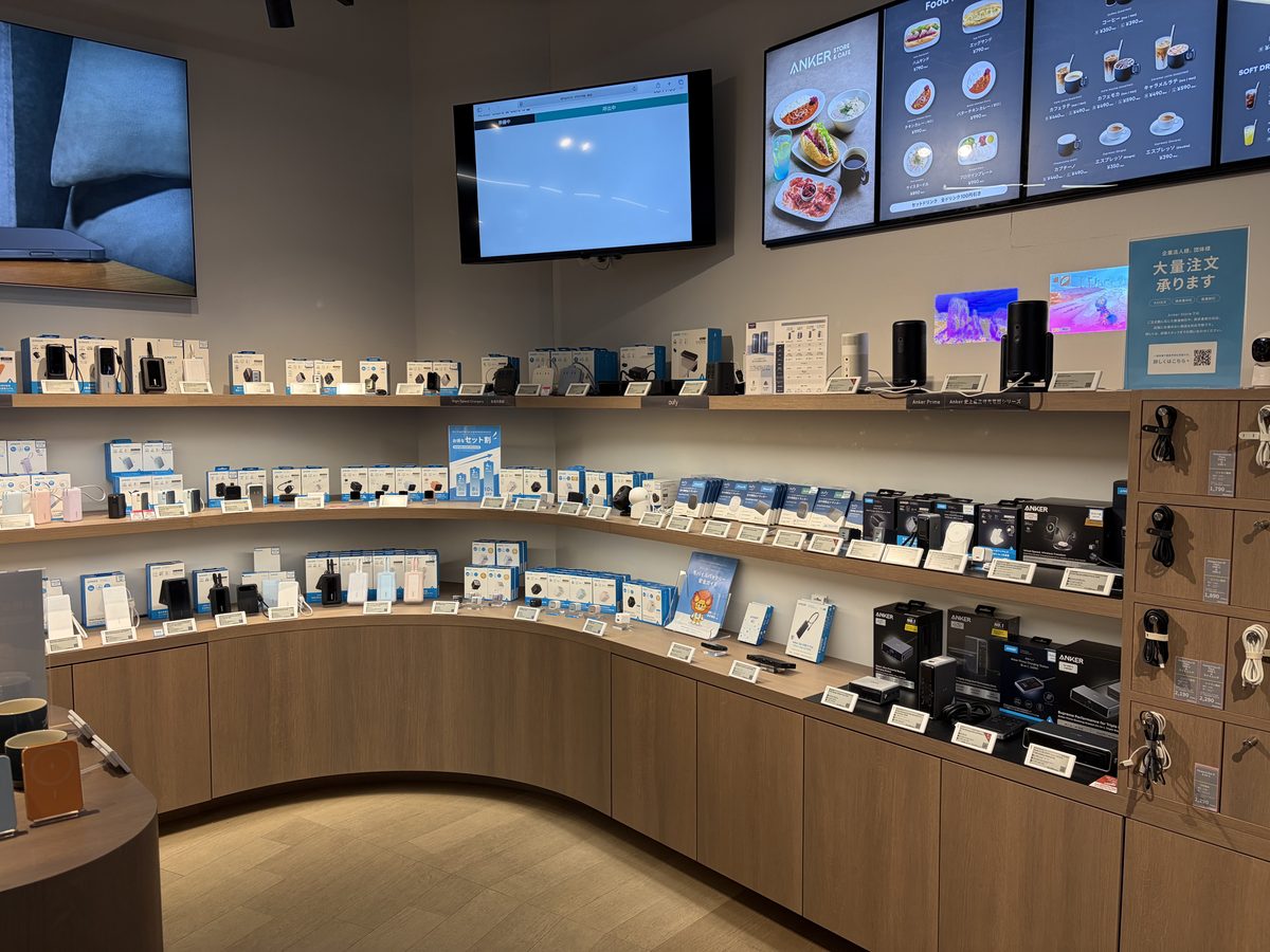 Anker Store 汐留の売り場全景。曲線の棚に充電器・バッテリーが並び、上部にカフェメニューのディスプレイ